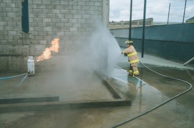 İtfaiyeci, bir gaz tankını söndürmek için yangın hortumuyla su perdesi oluşturuyor.
