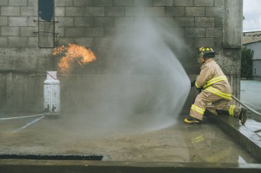 İtfaiyeci, bir gaz tankını söndürmek için yangın hortumuyla su perdesi oluşturuyor.