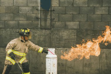 İtfaiyeci kıyafetiyle yanan bir benzin deposunun gaz akışını kahramanca kesiyor.
