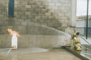 İtfaiyeci, bir gaz tankını söndürmek için yangın hortumuyla su perdesi oluşturuyor.