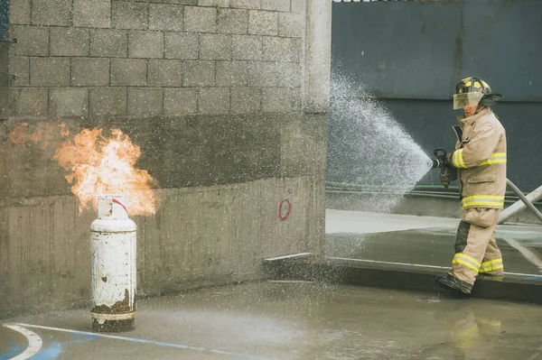 İtfaiyeci, bir gaz tankını söndürmek için yangın hortumuyla su perdesi oluşturuyor.