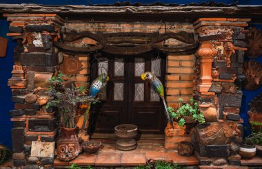 Geleneksel Meksika penceresinde kil figürler, renkli ahşap papağanlar ve bazı bitkiler var.