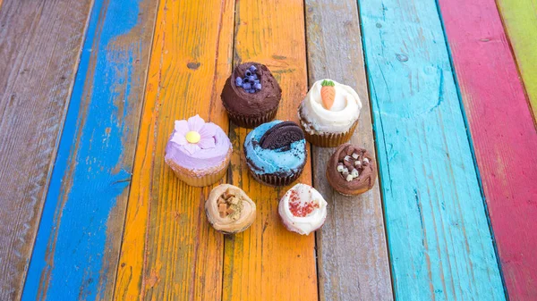 Πολύχρωμα Και Νόστιμα Cupcakes Ένα Πολύχρωμο Ξύλινο Τραπέζι Εικόνα Αρχείου