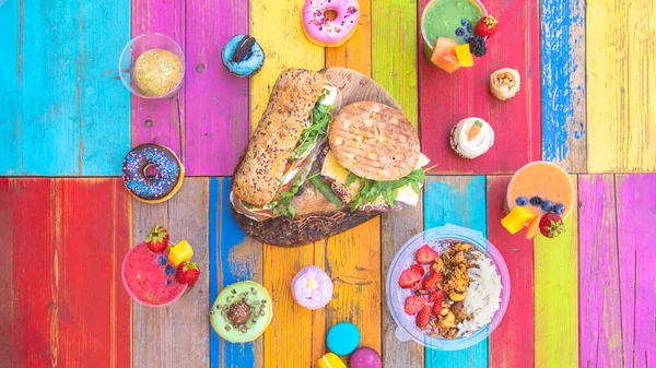 色彩斑斓的酒水 色彩艳丽的木桌上摆满了平底锅 纸杯蛋糕 甜甜圈和三明治的蜗牛 图库图片