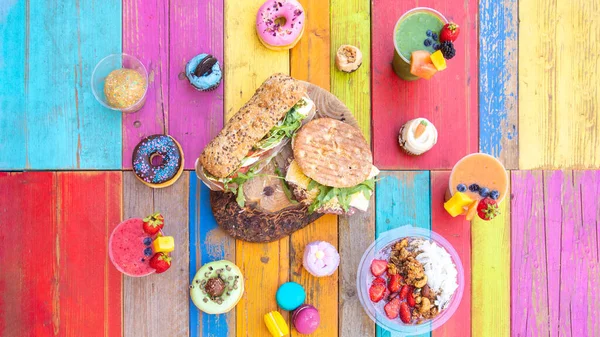色彩斑斓的酒水 色彩艳丽的木桌上摆满了平底锅 纸杯蛋糕 甜甜圈和三明治的蜗牛 免版税图库照片
