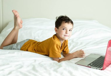 Yatak odasında dizüstü bilgisayarı olan gülümseyen küçük çocuk.