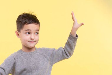 Beyaz bir çocuğun portresi hoş bir jest yapıyor, elinin kenarına bakıyor. Sarı stüdyo arka planında izole edilmiş. Mesaj için yer. 2021 için moda renk kombinasyonu. Reklam kavramı.