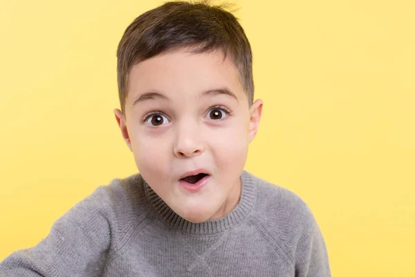 Heyecanlı, şaşırmış çocuk sarı stüdyo arka planında. İlkokul çocuğu. Göz teması, komik bir ağız. Kapalı yüz portresi, izole edilmiş. Pozitif duygular, parlak fikir, yüz ifadesi konsepti.