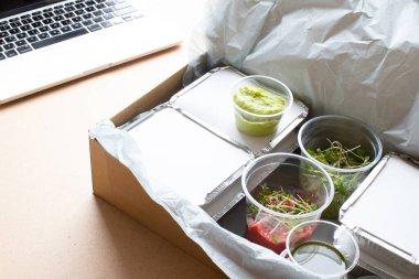 Yemek teslimatı, sağlıklı yeme konsepti. Masadaki konteynırlarda güzel vejetaryen yemekleri ve arka planda dizüstü bilgisayarlar.