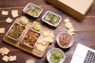Yemek teslimatı konsepti, sağlıklı yemek. Lezzetli, güzel vejetaryen Asya yemekleri, ahşap arka planda paket servis kutularında. Üst Manzara. Tayland eriştesi, vegan humusu. Yatay olarak. Hiç kimse. Boşluğu kopyala.