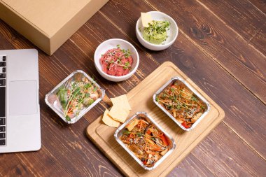 Yemek teslimatı konsepti, sağlıklı yemek. Lezzetli, güzel vejetaryen Asya yemekleri, ahşap arka planda paket servis kutularında. Üst Manzara. Tayland eriştesi, vegan humusu. Yatay olarak. Hiç kimse. Boşluğu kopyala.