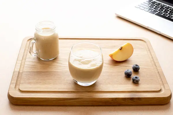 Concept for food blogging, online culinary masterclass. Fresh smoothie in a glass on a wooden cutting board next to a laptop. Copy space. Mockup.