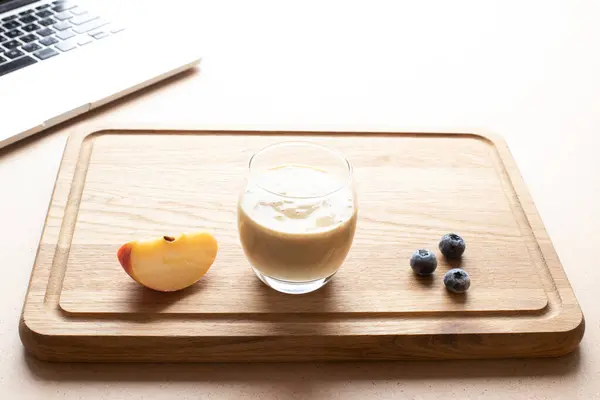 Concept for food blogging, online culinary masterclass. Fresh smoothie in a glass on a wooden cutting board next to a laptop. Copy space. Mockup.