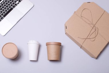 Teslimat, internetten ofise yemek sipariş etmek, yoğun bir gün, çevre dostu ambalaj, fast food konsepti. Çeşitli yiyecek kutuları, pizza için karton kutular, gri arka planda dizüstü bilgisayarlar. Düz yatıyordu.