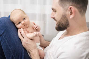 Sakallı mutlu baba kucağında yeni doğmuş bir bebek tutuyor. Evdeki kanepede oturuyor. Ebeveynlik kavramı, babalık, çocuk hayatının ilk ayları.