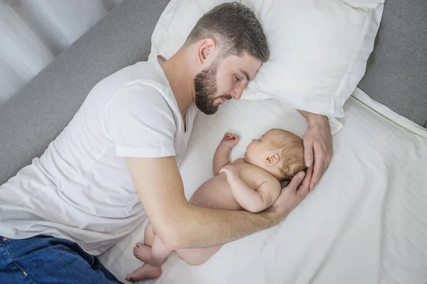 Happy dad hugs his naked newborn son. Sleep together at home lying on the couch. Lifestyle. The concept of parenting, fatherhood, tenderness, love.