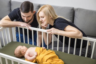 Yeni doğmuş bebeğiyle mutlu bir aile, güzel sarı bir bezle kaplı bir beşikte yatıyor. Yeni yaşam tarzı konsepti. Evdeki aile hayatının otantik duygusal anı. Beyaz ırk. 