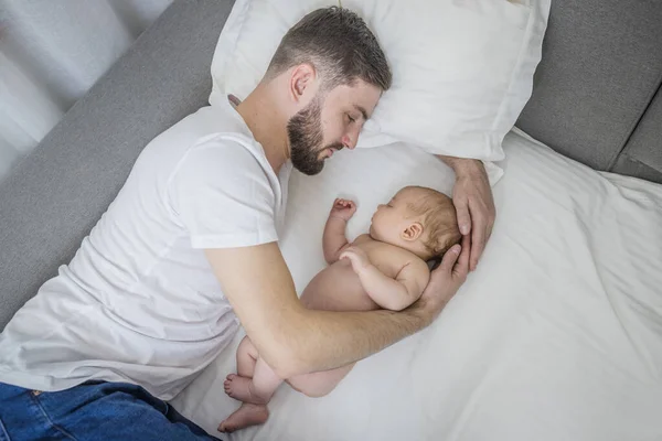 Happy dad hugs his naked newborn son. Sleep together at home lying on the couch. Lifestyle. The concept of parenting, fatherhood, tenderness, love.