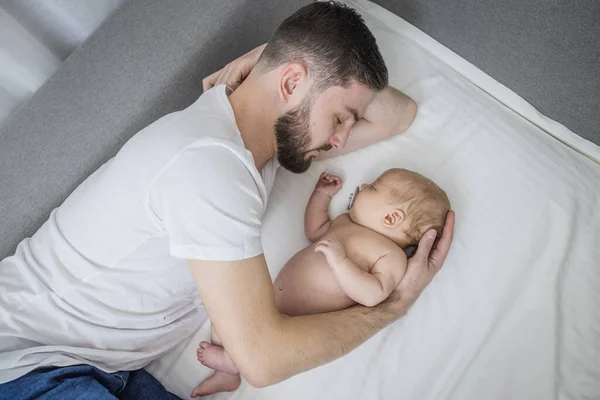 Happy dad hugs his naked newborn son. Sleep together at home lying on the couch. Lifestyle. The concept of parenting, fatherhood, tenderness, love.