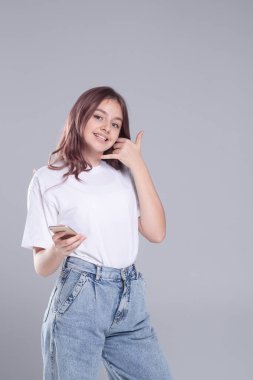 Akıllı telefonlu hoş bir kız bana bir jest yaptı. Göz teması. Stüdyo ışığı, gri arka plan. Kafkasyalı. Beyaz tişört ve kot pantolon giymişti. Reklamcılık, sosyal ağlar, online pazarlama kavramı.