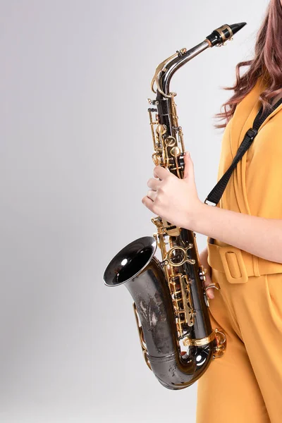 Hands of a young girl are holding a golden saxophone. Concept jazz, blues, rock-n-roll, saxophone training courses, musician, hobbies, sounds of music. Vertical. Copy space. Studio light. Caucasian.
