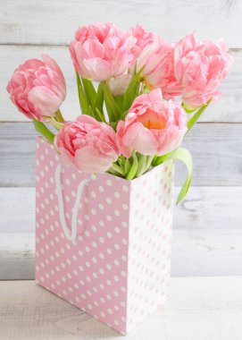 Güzel bir buket taze gerçek lale pembe noktalı bir hediye çantasının içinde duruyor, beyaz tahta arka planda. Mutlu yıllar, hediyeler, anneler günü, sevgililer günü, 8 Mart, bahar alışverişi, bahar zamanı konsepti. Dikey.