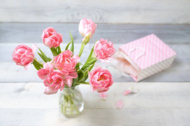 Beyaz tahtaların üzerinde şirin hediye çantasının yanında vazodaki güzel pembe laleler. Bahar buketi kavramı, 8 Mart, kadınlar günü, ilkbahar, şenlik havası, anneler günü, bayram, mutlu yıllar..