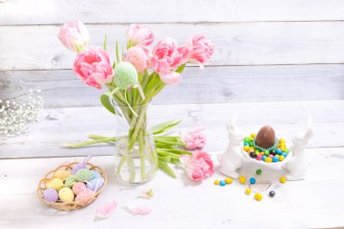 Vazoda saklı yumurtalar ve taze bahar laleleri olan Paskalya dekoru. Süslü Paskalya tavşanı, arka planda bir sürü renkli yumurta. Paskalya gelenekleri, bahar, çiçek, tatil.