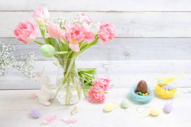 Vazoda saklı yumurtalar ve taze bahar laleleri olan Paskalya dekoru. Süslü Paskalya tavşanı, arka planda bir sürü renkli yumurta. Paskalya gelenekleri, bahar, çiçek, tatil.