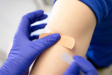 Covid-19 aşısı, sağlık hizmeti konsepti. Doktorun mavi eldivenli elleri enjeksiyon bölgesini tedavi ediyor. Aşıdan sonra hastaya sıva yapıştırıyor. Kapatın. Yatay.