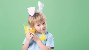 Küçük tatlı duygusal çocuk nazikçe yumurta ve tavşan kulaklı dekoratif yuvayı tutuyor. Yeşil stüdyo geçmişi. Kopya alanı olan Paskalya kartı. Paskalya geleneği, yumurta avcısı kavramı. Göz teması. 