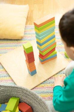 Child preschooler plays on a striped carpet with colored wooden cubes, building blocks, learns new skills at home or in kindergarten. Concept of toys from eco materials, the development of creativity.