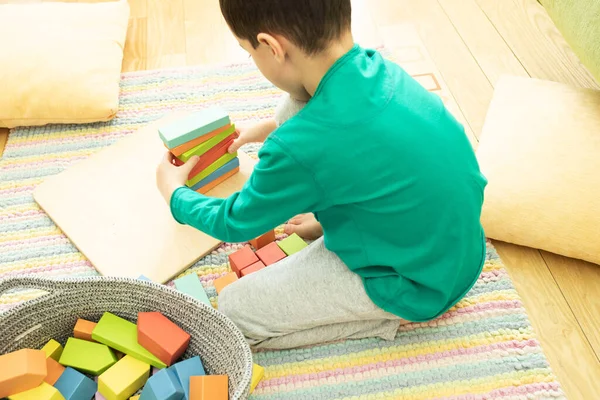 Child preschooler plays on a striped carpet with colored wooden cubes, building blocks, learns new skills at home or in kindergarten. Concept of toys from eco materials, the development of creativity.
