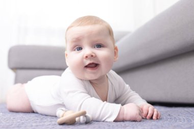 Yenidoğan bebek, başını karnının üzerinde iyi tutuyor, çıngırakla temas halinde. Evde, koltuğun yanında, yerde. Bebek bakımı, ebeveynlik, 0-6 aylık bebek gelişimi