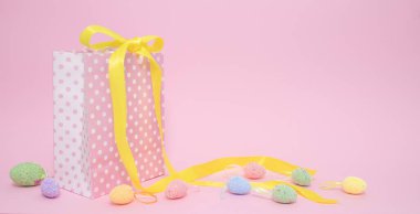 Noktalar halinde hediye paketi, şenlikli sarı kurdeleyle bağlanmış ve pembe arkaplanlı renkli yumurtalar ve fotokopi alanı. Paskalya indirimi. Pastel renk tasarımı. Hiç kimse. Yatay Pankart.