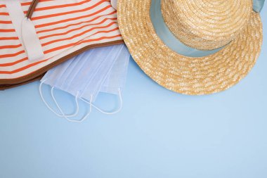 Modaya uygun hasır şapka, tıbbi maske, mavi arka planda çizgili plaj çantası. Bir salgın sırasında denize yolculuk, koronavirüs konseptini önlemek için yeni kurallar. Düz yat, boşluğu kopyala.