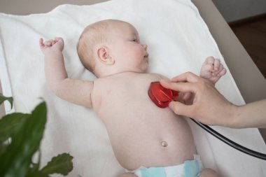 Yeni doğmuş bir bebeği olan bir çocuk doktoru. Steteskoplu bir kadın eli bebeğin nefesini dinler. Çocuğun sağlıklı gelişim kavramı, rutin muayene, hastalık tanısı, nefes alma, akciğerler.