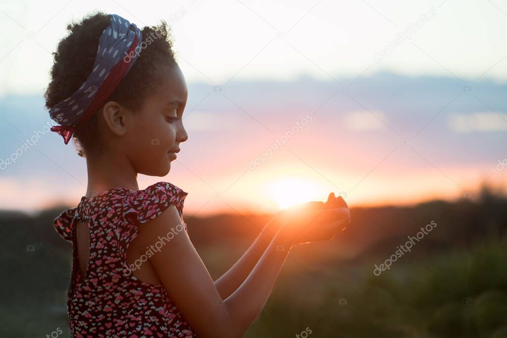 Girl at sunset. African American child holds the sun in his palms. Against the background of the landscape. Mixed race, Afro hair. The concept of happiness, dreams, stop racism, travel. Life style.