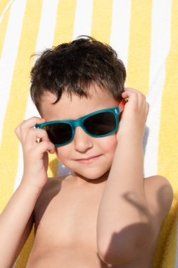 Güneş gözlüklü mutlu çocuk, yaz tatilinin tadını çıkarıyor. Seyahat kavramı, ultraviyole radyasyondan göz koruması, şık çocuk gözlüğü. Pazar.