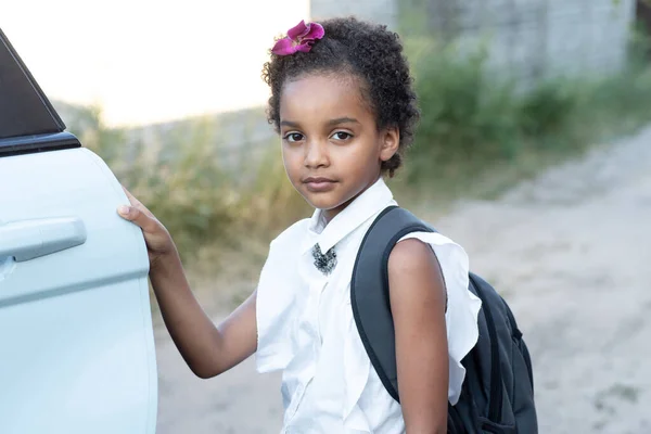 車のドアの近くに学校のバックパックを持つアフリカ系アメリカ人の子供 アフリカの髪をした可愛い女子高生 学校に戻るための概念 子供の安全 ライフスタイル — ストック写真