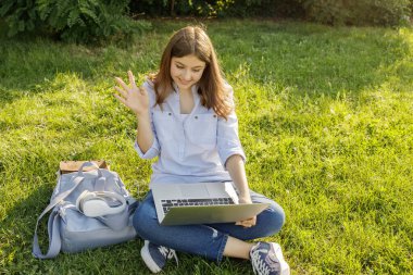 Parkta dizüstü bilgisayarı olan mutlu bir genç kız. Liseli kız dışarıda internetten iletişim kuruyor, hoş bir jest yaptı. İnternetteki arkadaş kavramı, uzaktan öğrenme, modern okul, online konferans