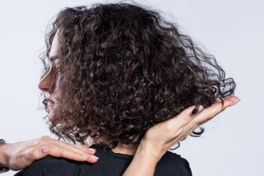 Siyah elbiseli güzel bir kızın yakın plan profil fotoğrafı, bir kuaför doğal buklelerle saç stili yapmış. Eller saç kesiminin açısını gösteriyor. Kuaförlük eğitimi.