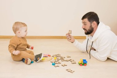 Aile kavramı, babalık, erken çocuk gelişimi - mutlu baba ve çocuk İngiliz alfabesinin tahta harfleriyle oynuyorlar. Babam, tahta zeminde yatarken bebek mektubunu gösteriyor..