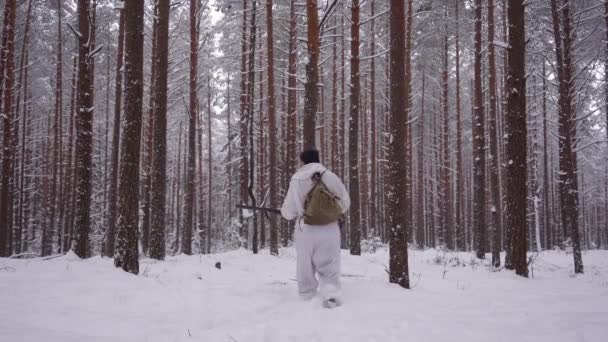 En jæger i camouflage tøj med en pistol går gennem vinterskoven i jagtsæsonen. – Stock-video
