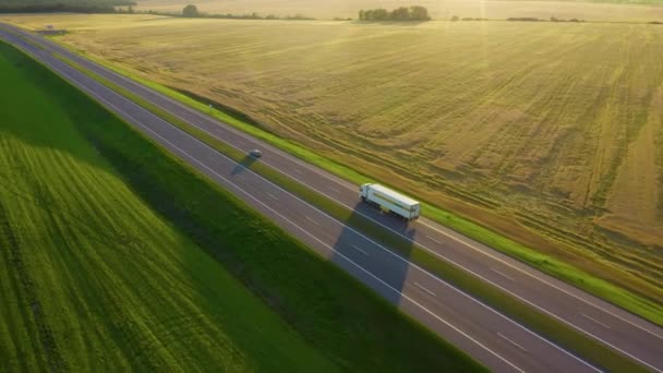 AEREO: Volare lungo un camion merci che trasporta merci attraverso la pittoresca campagna all'alba dorata. Il camion guida le merci verso un centro logistico in campagna in una soleggiata serata estiva. — Video Stock