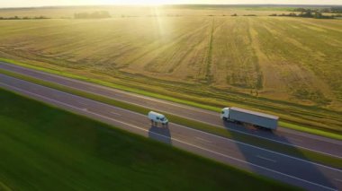 Hava görüntüsü: araçlar, kamyonlar ve araçlar yolda gidiyor. Günbatımı yaz zamanı.