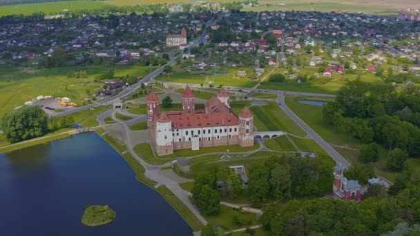 Mir, Bělorusko. Letecký pohled na quadcopter hradu Mir v Bělorusku, který se nachází v obci Mir, obklopen stromy a nachází se v blízkosti malého jezera. — Stock video