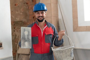 Kürekçi ve beton sepetli tuğla ustası kameraya bakıyor.