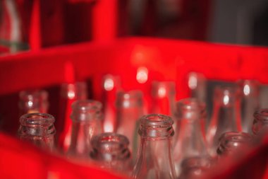 Şişeler kırmızı plastik bir kutunun içinde. Boş cam şişelerin boyunları. Karbonatlı içeceklerin altındaki cam kaplar.