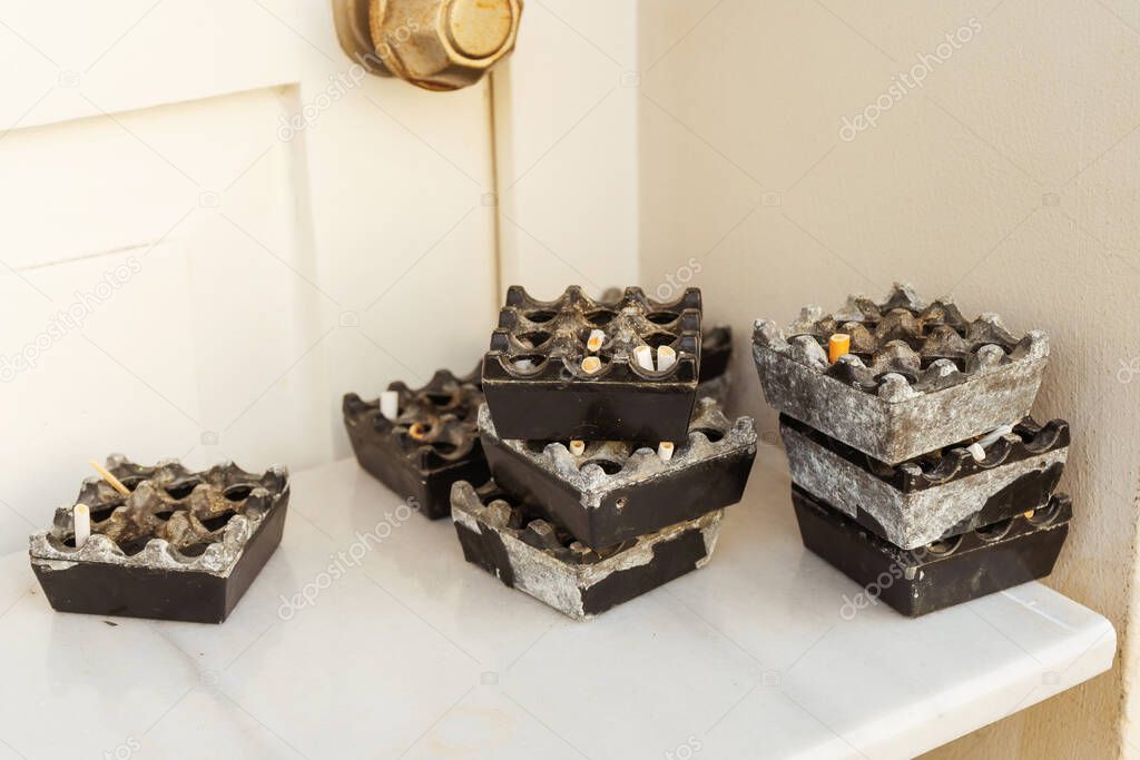 Ashtrays with cigarette butts on a white table. Dirty ashtrays in the shape of a square. A pile of used ashtrays in a cafe